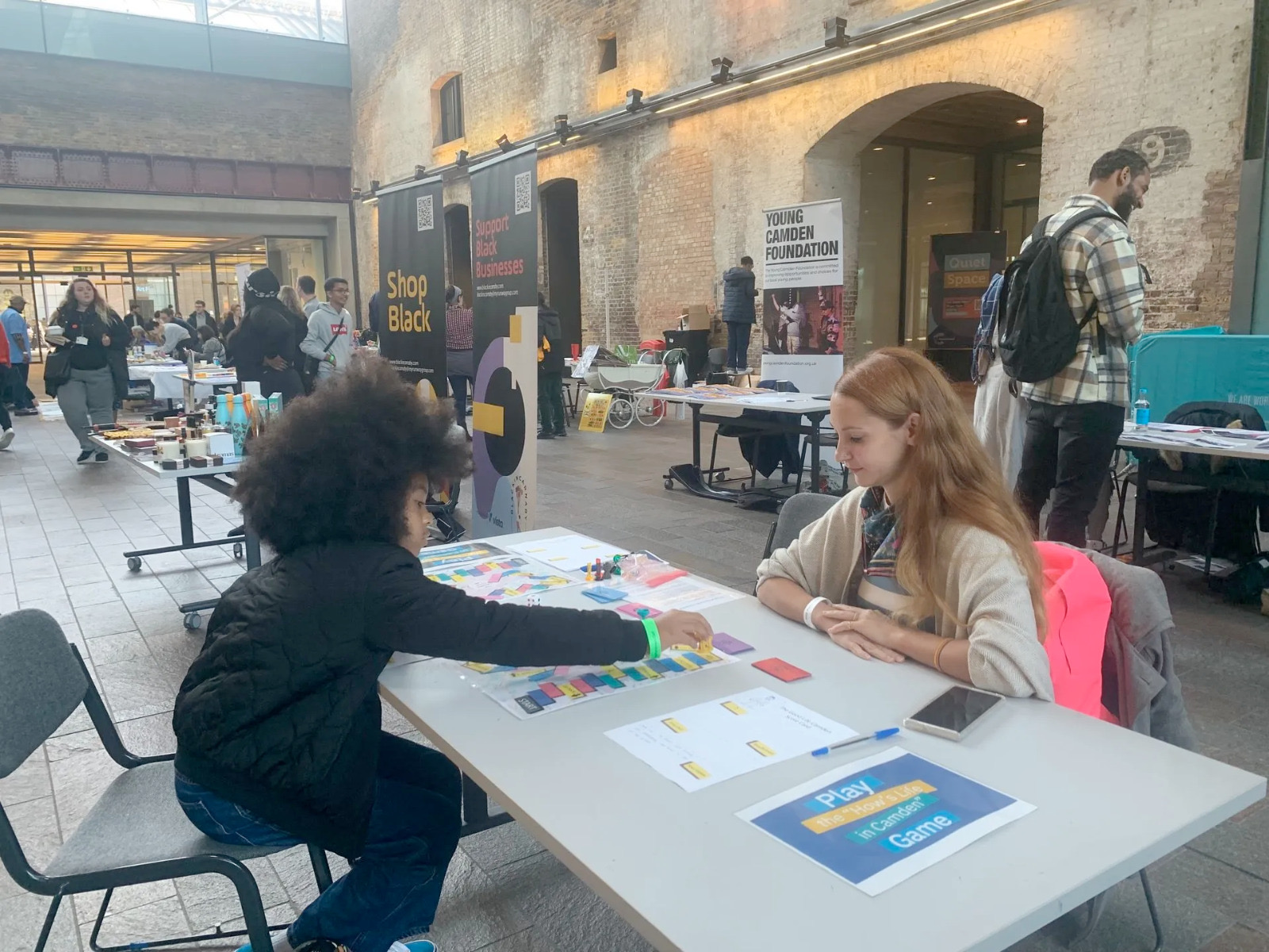 Nikolett Puskás facilitating the &lsquo;How&rsquo;s Life in Camden&rsquo; Game with a young participant in a Camden community space.
